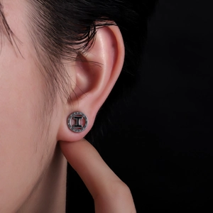 Gros plan d'un clou d'oreille en acier titane argenté avec logo H noir sur un mannequin