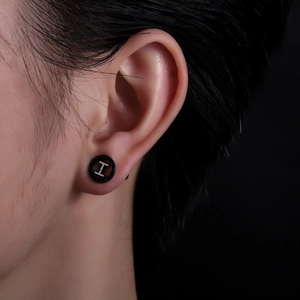 Gros plan sur un clou d'oreille rond noir en titane avec un design de lettre H argentée