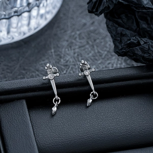 Macro detail of silver sword-shaped stud earrings with micro diamonds and leather background