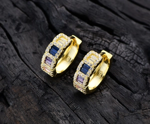 Close-up of S925 gold-plated earrings with rectangular multicolor crystals on dark wood