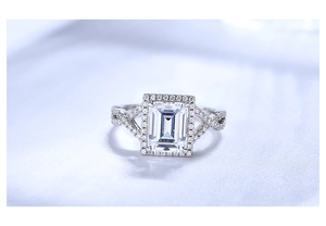 Macro shot of 7x9 emerald cut halo engagement ring with intertwined pave silver band