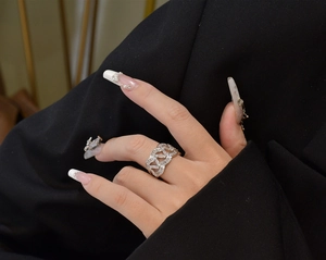Gros plan d'une bague chaîne en argent avec zircons sur main de femme et fond sombre