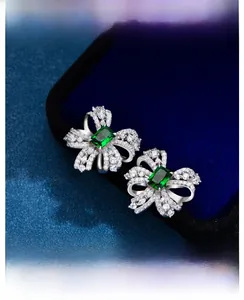 Close-up of silver bow earrings with emerald stones and zircon accents on blue velvet