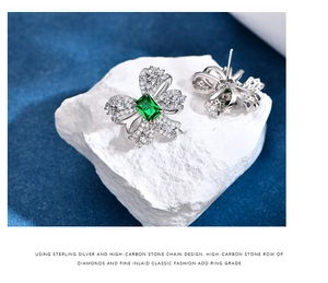 Macro shot of silver bow earrings with emerald gemstone on a stone surface