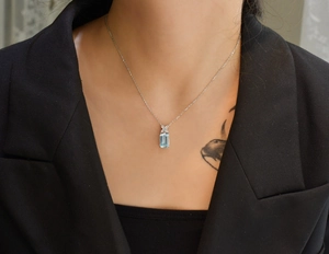 Close-up of a silver chain necklace with a rectangular aquamarine pendant on a model