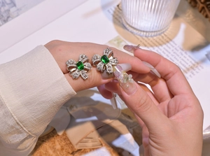 Detail of emerald cut green gemstone bow earrings in silver on a hand