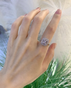 Detailed view of emerald cut halo engagement ring with pavé diamond band on hand