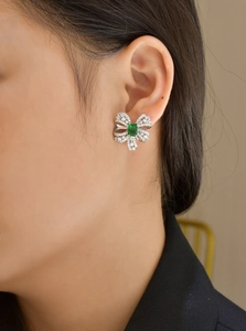 Close-up of bow earrings with emerald gemstone and pave diamonds on model's ear