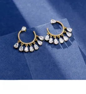 Close-up of gold drop earrings with pear-cut crystals and pavé stones on a blue surface