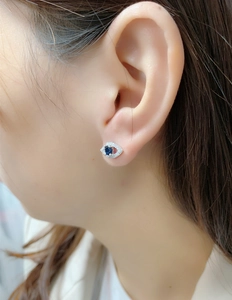 Close-up of a S925 sterling silver evil eye stud earring with blue sapphire on a model ear