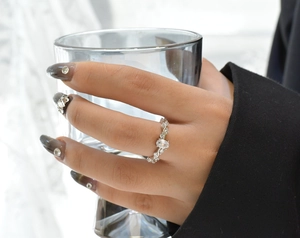 Detail view of silver wavy ring with oval cubic zirconia on hand holding a glass