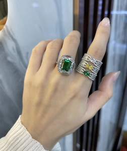 Detalle de anillo de esmeralda y alianzas de plata apilables en la mano de modelo
