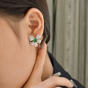 Silver bow stud earrings with emerald stone and pavé zircon worn by a model