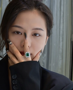 Emerald cut green gemstone ring with halo diamonds worn by a model in a black suit