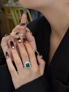 Macro shot of an emerald-cut green gemstone ring with marquise-cut accents on a hand