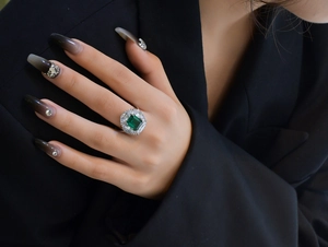 Close-up of a luxury emerald-cut green gemstone ring worn on hand with black outfit