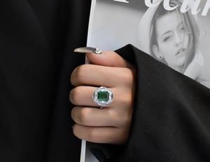 Macro view of emerald-cut green gemstone ring with marquise zircon halo on hand