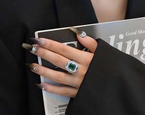Macro shot of an emerald-cut green stone ring with marquise zircon halo on a model hand