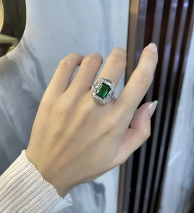 Close-up of emerald cut green stone ring with pavé diamonds on a hand model