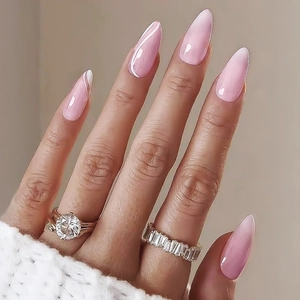 Macro view of long almond pink glossy press-on nails shown on a hand with elegant rings