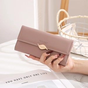 Gros plan du long portefeuille élégant en cuir rose poudré avec un fermoir feuille doré