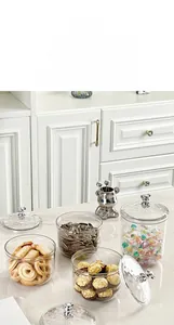 Detail of clear glass storage jars with creative silver bear handles on white marble