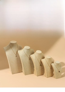Detailed view of beige linen necklace display busts in tiered arrangement with gold chains