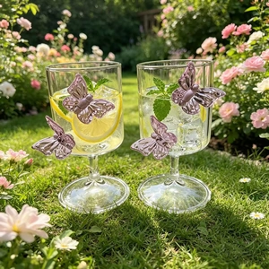 Detail view of two glass champagne flutes with purple butterfly accents in an outdoor garden