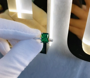 Macro shot of emerald-cut green stone ring with pavé-set crystals on silver band