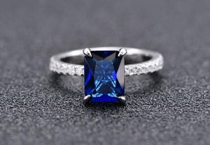 Macro detail of emerald-cut blue sapphire ring with 4-prong setting and side accents