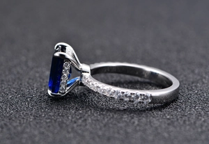 Detailed macro view of silver ring with 7x9mm emerald-cut blue gem and pavé zircon setting