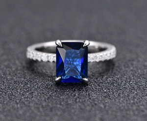 Macro view of a deep blue rectangular emerald-cut gemstone in a four-prong silver setting