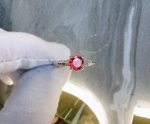 Macro shot of a four-prong red gemstone silver ring with leaf accents held in a gloved hand