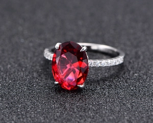 Macro shot of oval-cut red gemstone ring in silver claw setting with micro-pave crystals