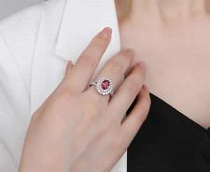Vue macro d'une bague rubis ovale avec double halo de diamants portée au doigt