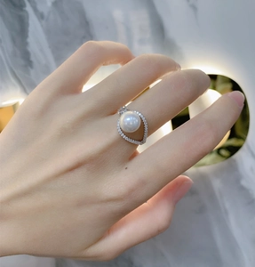 Close-up of a 925 silver pearl ring with teardrop diamond halo design on a model finger