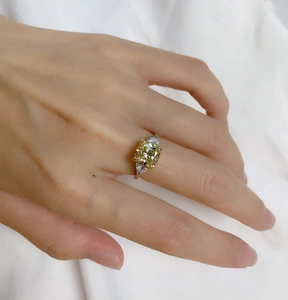 Macro view of cushion-cut yellow gemstone ring with pear-shaped side diamonds on finger