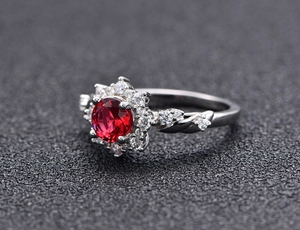 Close-up of four-claw silver ring with a red gemstone and sparkling diamond halo