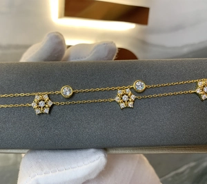 Detail eines goldenen Schichtarmbands mit Schneeflocken-Charm und Zirkon-Steinen