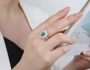 Close-up of S925 silver pear-cut green emerald ring on a model holding a magazine