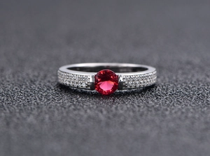 Macro shot of S925 silver ring featuring a round red gemstone and pavé-set side diamonds