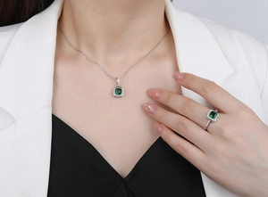 Detail of square emerald necklace and ring set on model in professional white suit
