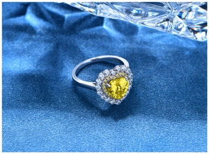 Top view of heart-shaped yellow gemstone ring with double-layered diamond halo on blue texture