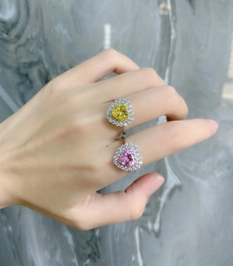 Close-up of heart-shaped pink and yellow halo rings on fingers with marble background