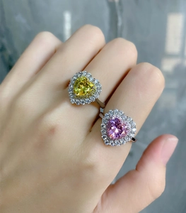Close-up of heart-cut pink and yellow rings with double halo settings on a hand