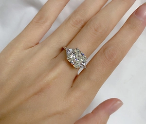Three-stone cushion cut sapphire ring with triangle side stones on a model's hand