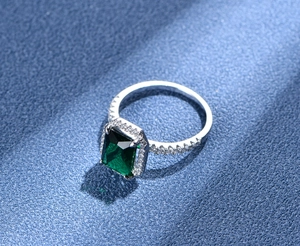 Vista macro dell'anello con gemma verde taglio rettangolare e halo di diamanti su blu