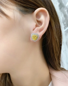 Close-up of heart-shaped yellow gemstone earrings with halo diamonds on a female model