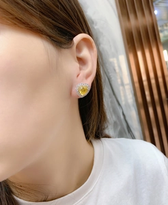 Close-up of heart-shaped yellow diamond earrings with halo setting on a model ear