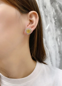 Close-up of heart-shaped yellow halo stud earrings worn on ear by a model